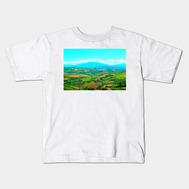 Scene in Carassai with fields sectoring the lands and impressive mountains Kids T-Shirt by KristinaDrozd